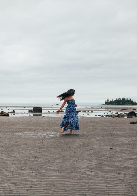 Minda Lane in a blue dress enjoying an intuitive energy healing session by the soothing waves of a sandy beach.