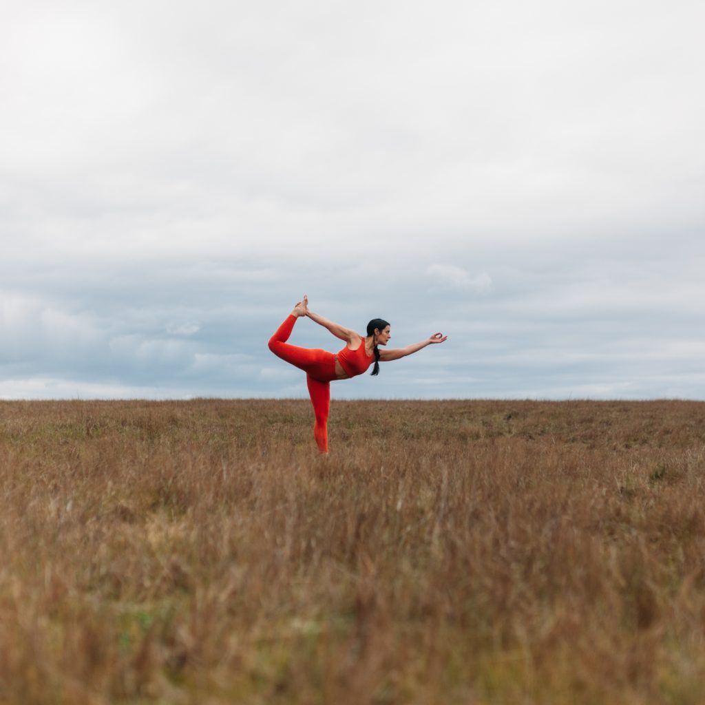Minda Lane, a woman in red, performing yoga in a serene field during her yoga class.
